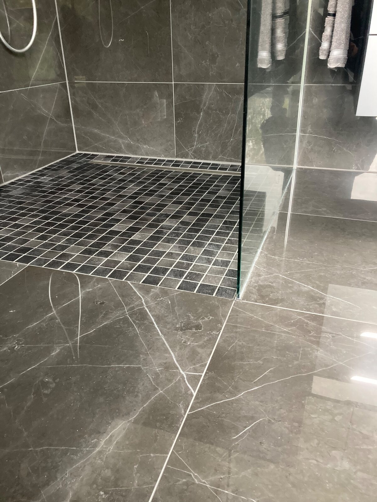 Bodengleiche Dusche mit dunklen Marmorfliesen und Mosaikboden – Referenz von Fliesen Sieke